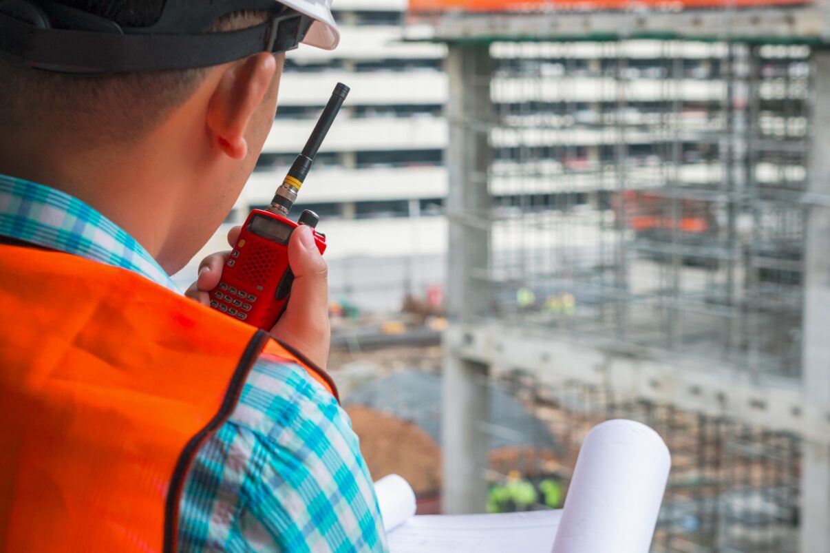 Man standing in safety gear with walkie-talkie looking out over construction site