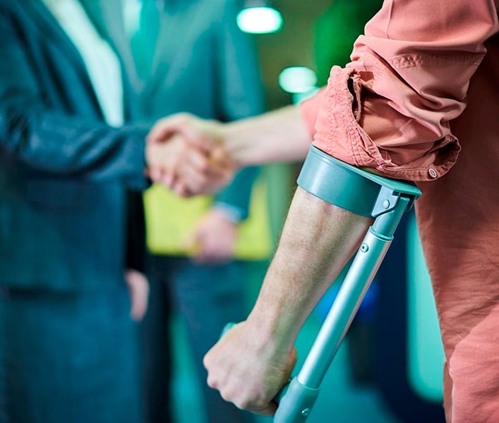 A man using a crutch, shaking another man's hand