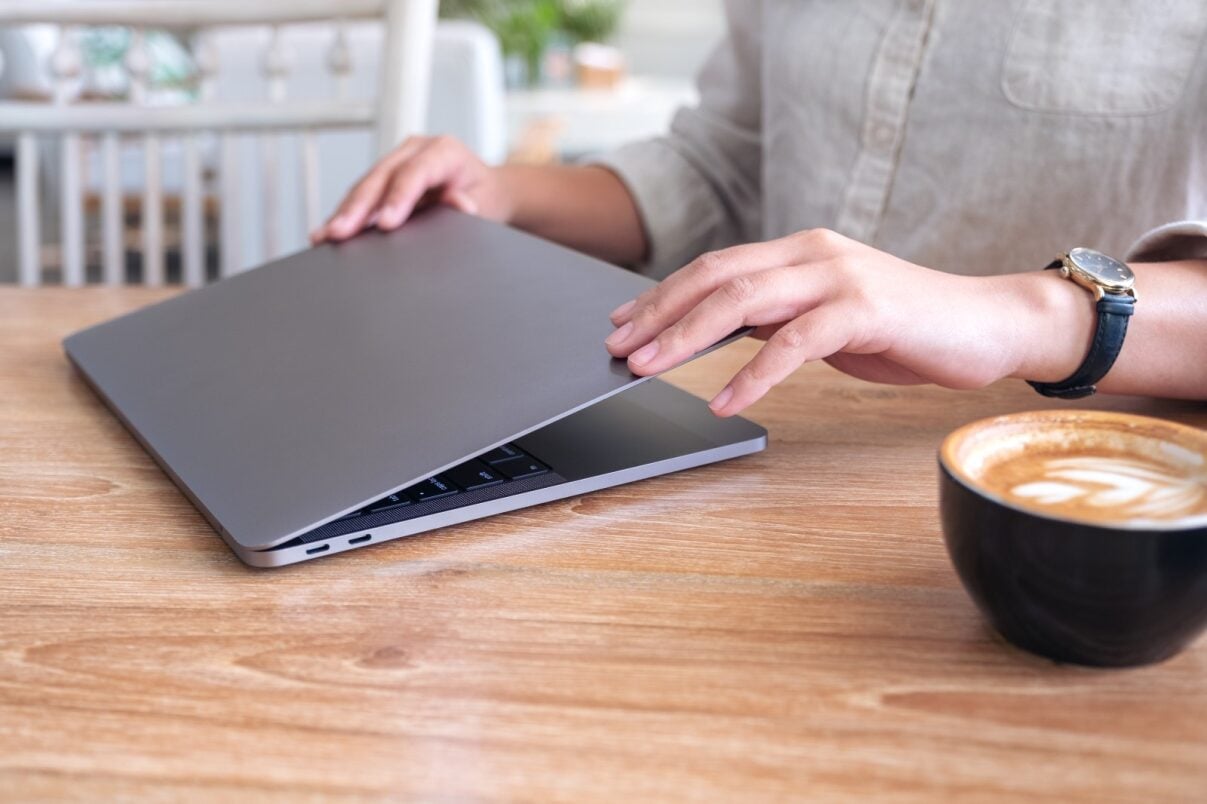 Man opening laptop on desk with coffee next to him