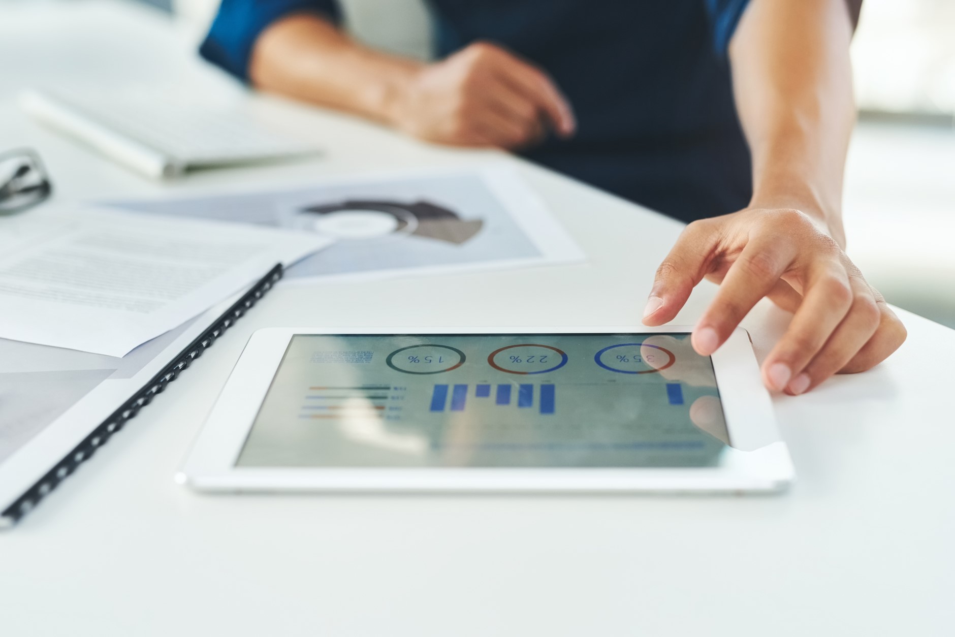 Woman on desk with paperwork looking at graphs on electronic tablet