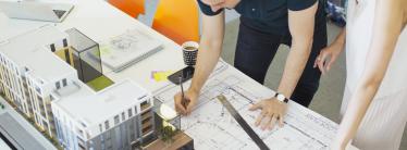 Two architects looking at plans and a model for an office building