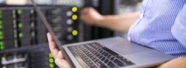 man holds laptop while adjusting dials on machinery