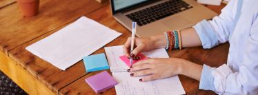 person at laptop writing in notebook with colourful sticky notes