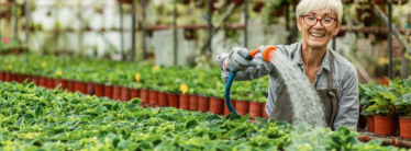 Older woman smiling while watering plants with a hose