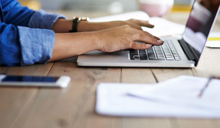 Person conducting business at a desk and typing on a laptop