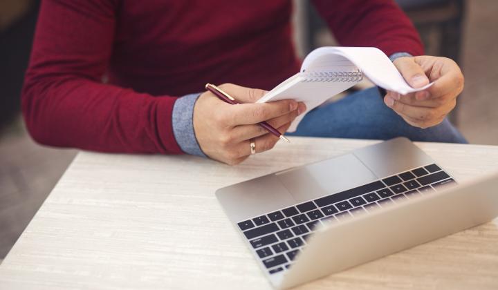 A man makes notes at his laptop