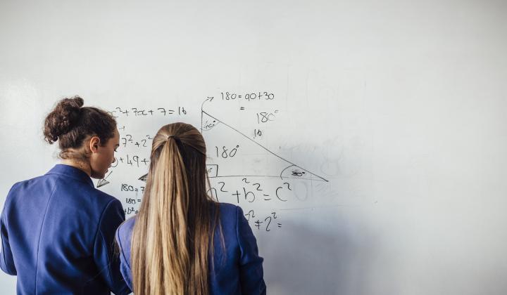 Two schoolgirls do maths on a whiteboard