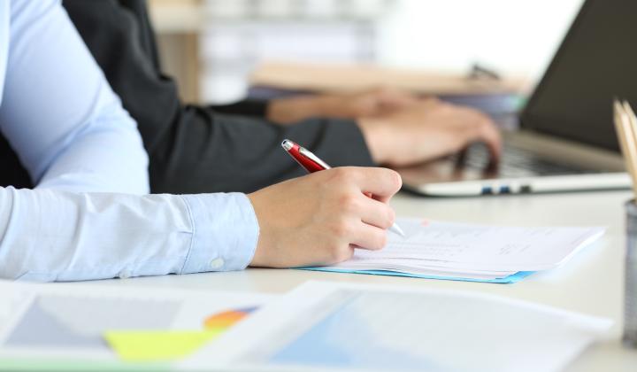 Two people working at a laptop and writing on paper