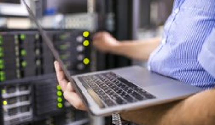 man holds laptop while adjusting dials on machinery