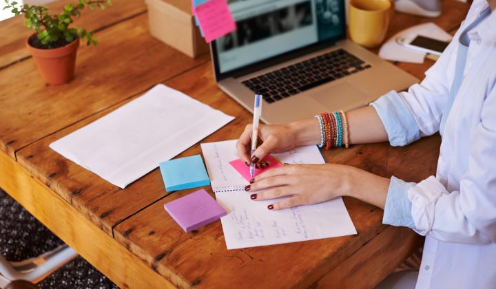 person at laptop writing in notebook with colourful sticky notes