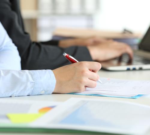 Two people working at a laptop and writing on paper