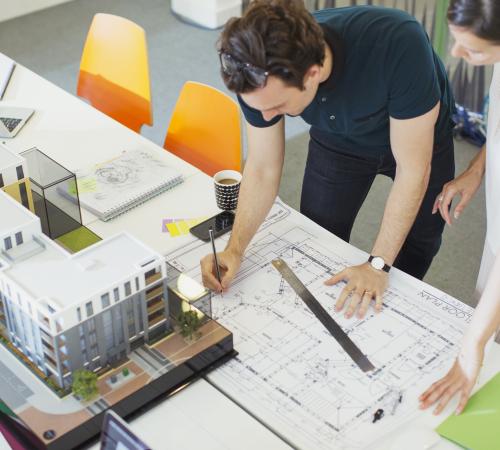 Two architects looking at plans and a model for an office building