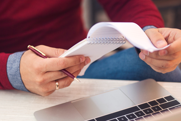 Man looking at notepad and laptop