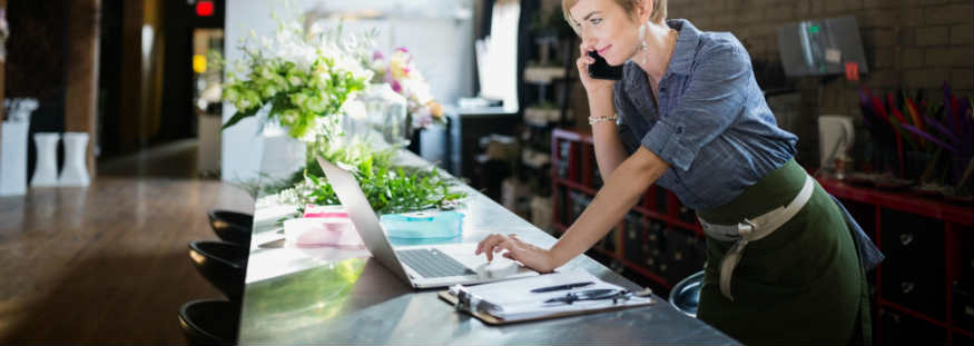 business owner on phone looking at laptop in workshop