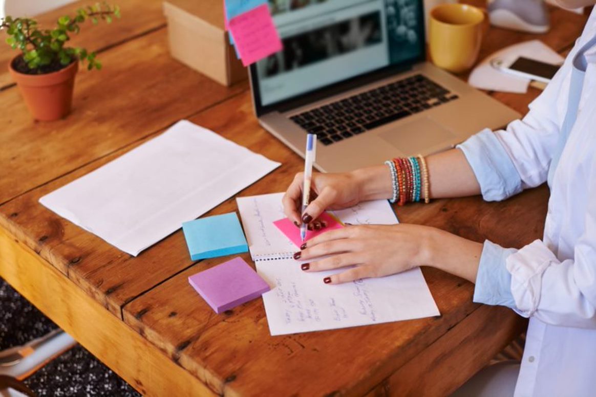 small business owner writing notes at laptop