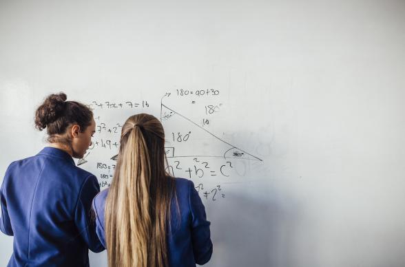 Two schoolgirls do maths on a whiteboard