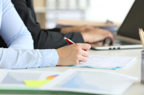 Two people working at a laptop and writing on paper